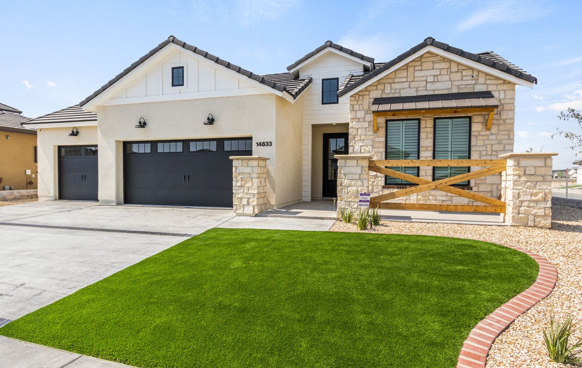 Modern home with beige stucco, stone accents, black garage doors, and a green lawn.