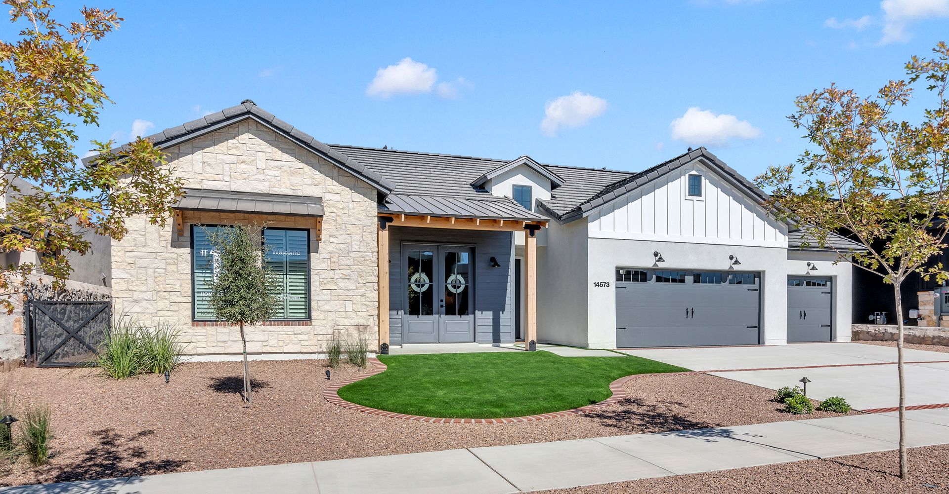 Modern single-story house with stone and white siding, gray garage doors, and a small green lawn.