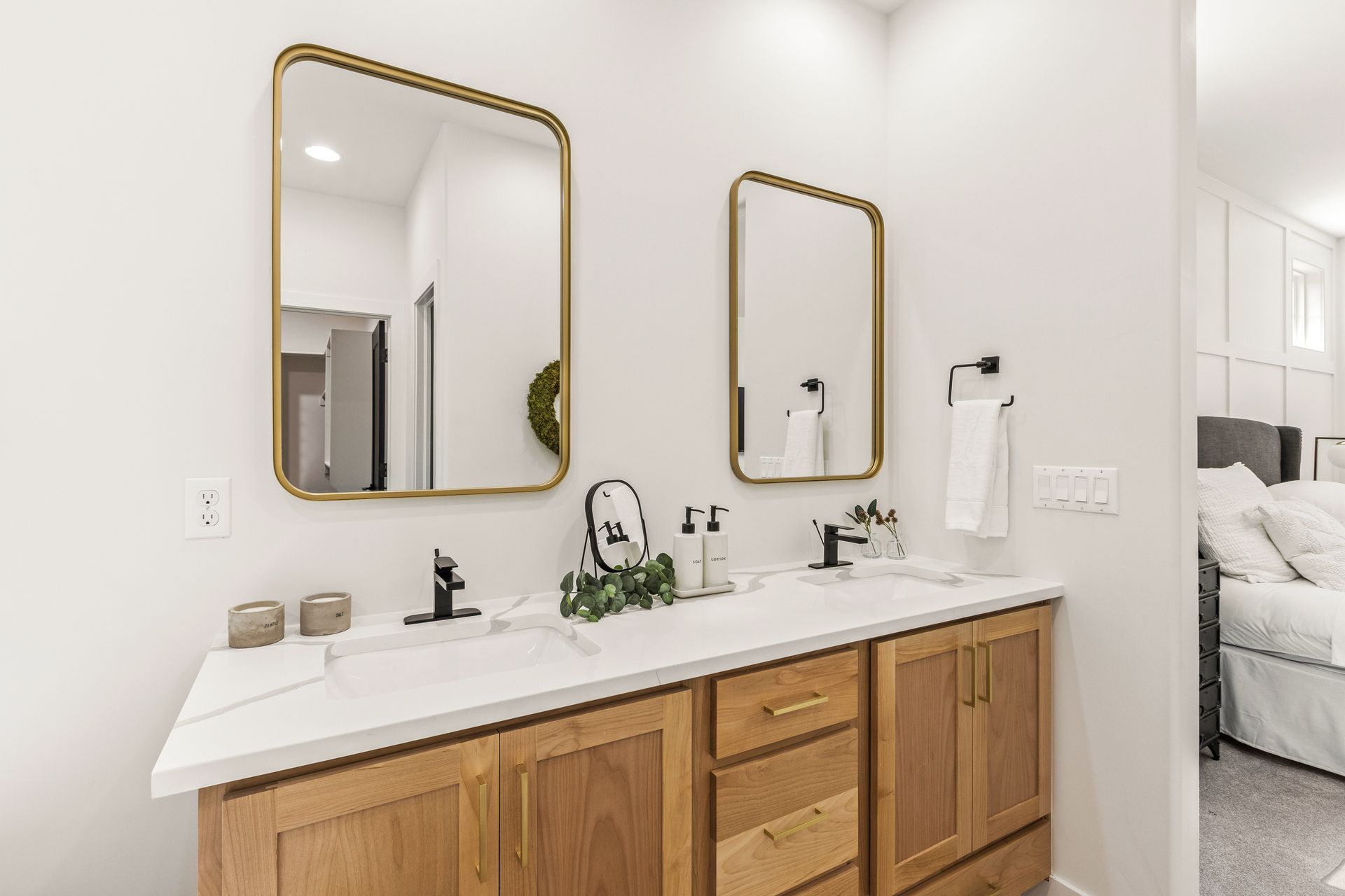 Bathroom with two sinks, gold mirrors, wooden cabinets, white countertop, and towel rack.