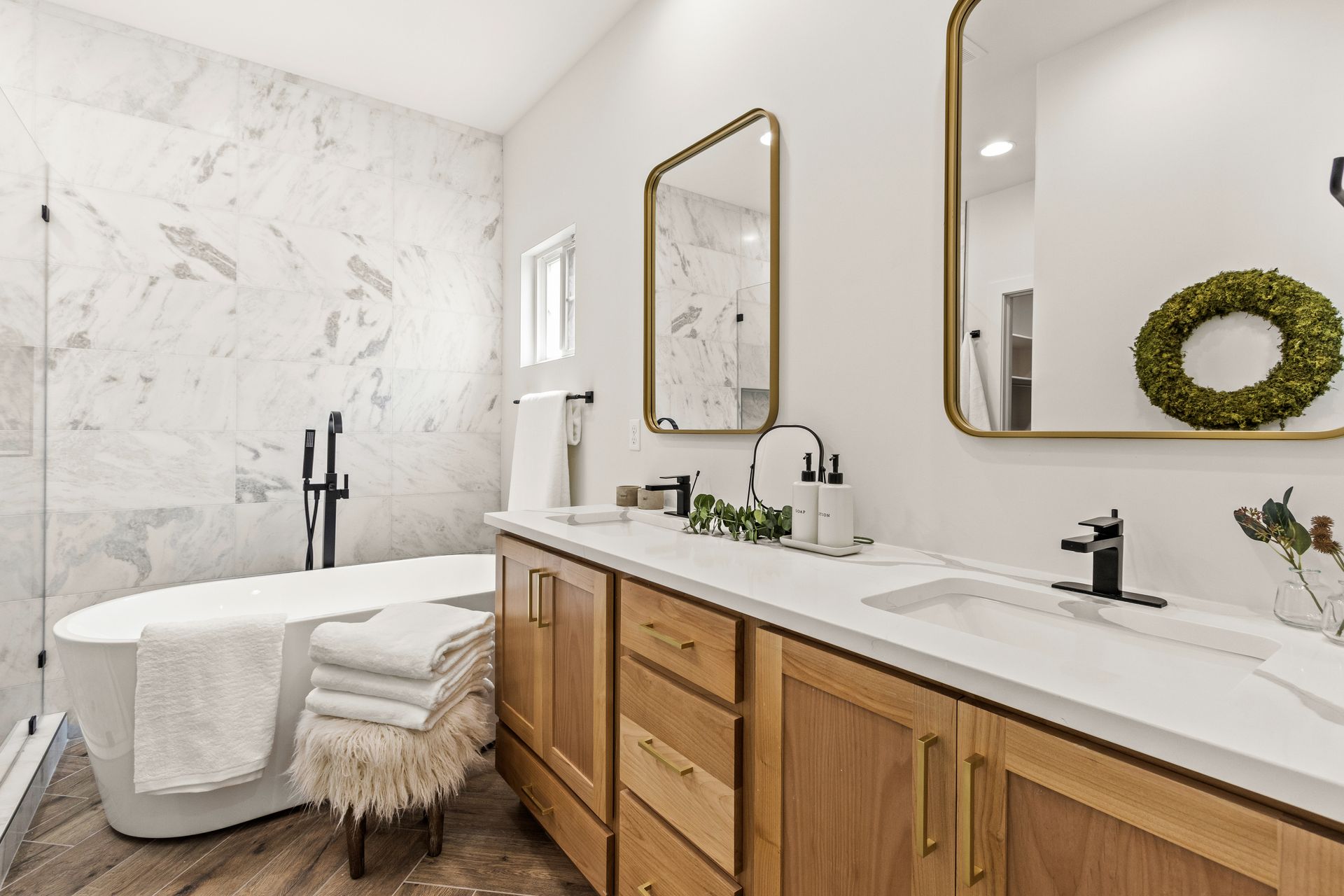 Bathroom with marble tile walls, a white tub, double vanity, and gold-framed mirrors.