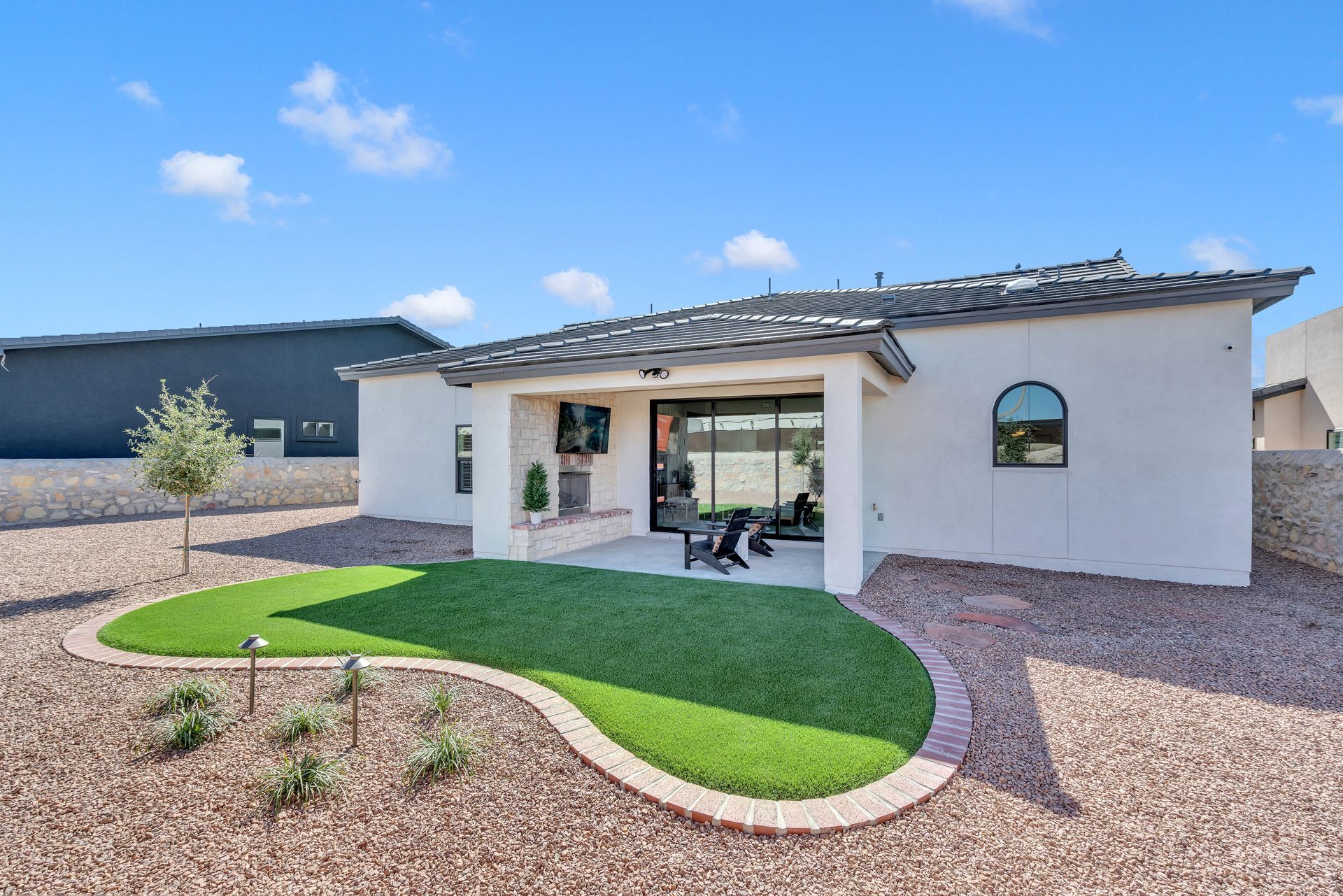 Backyard of a house with green lawn, covered patio, and gravel landscaping under a blue sky.
