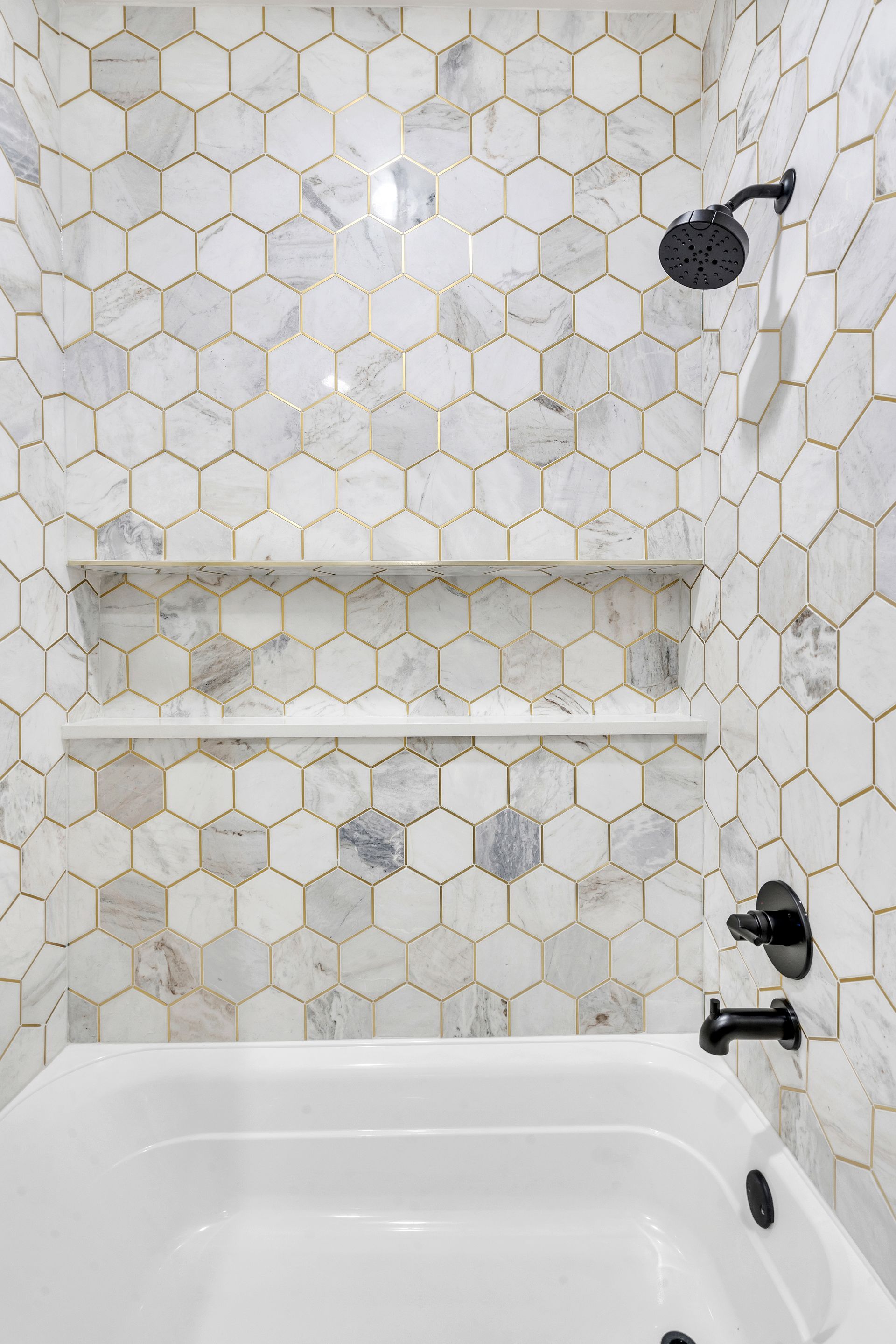 White hexagon tile shower with a built-in shelf and black fixtures.