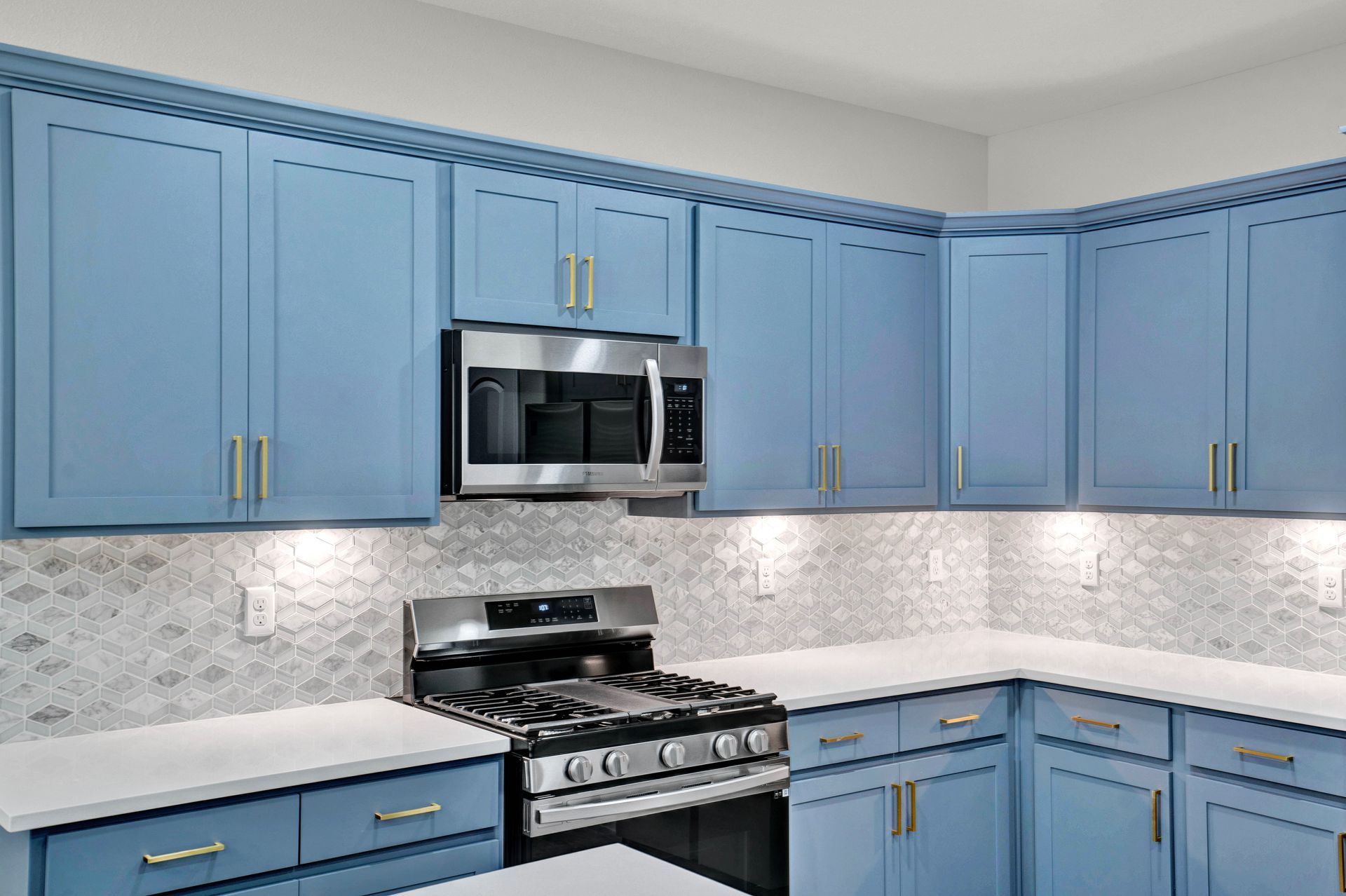 Blue kitchen cabinets with gold hardware, stainless steel appliances, and white countertops.