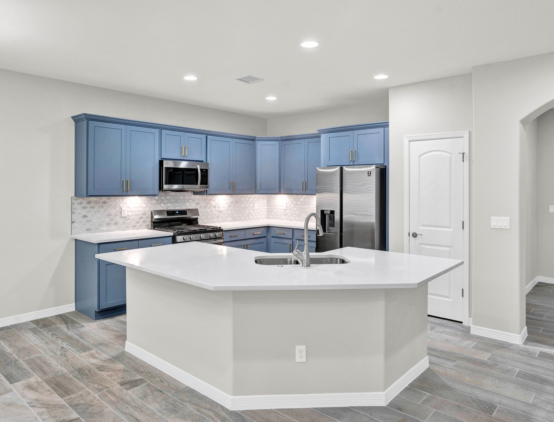 Blue kitchen cabinets with white countertops and island, stainless steel appliances.