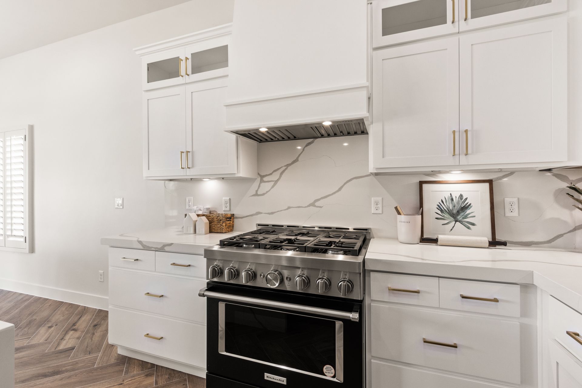 White kitchen with stove and cabinetry, marble backsplash and light wood flooring.