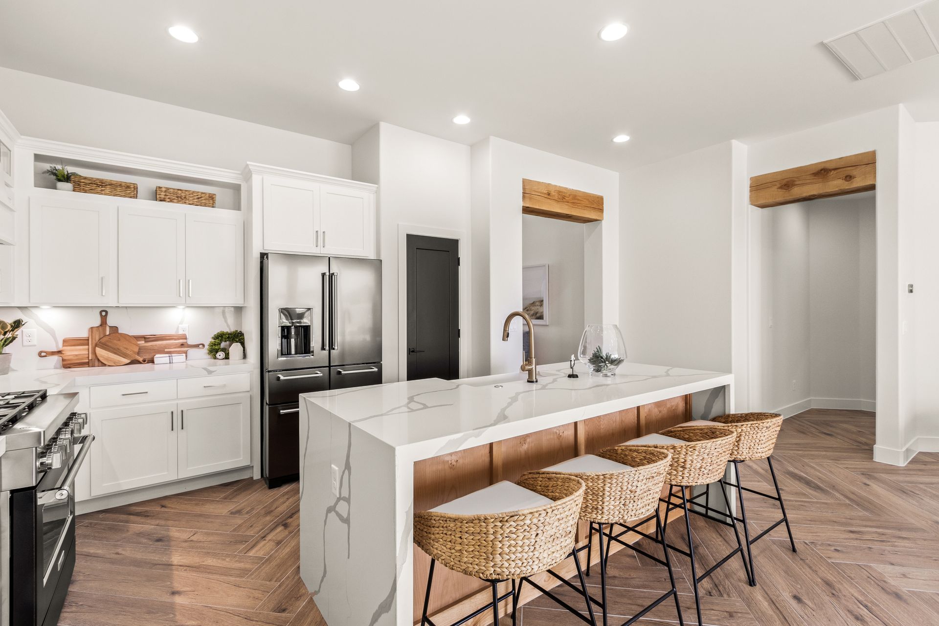 Modern kitchen with white cabinets, stainless steel appliances, and a marble island with woven bar stools.