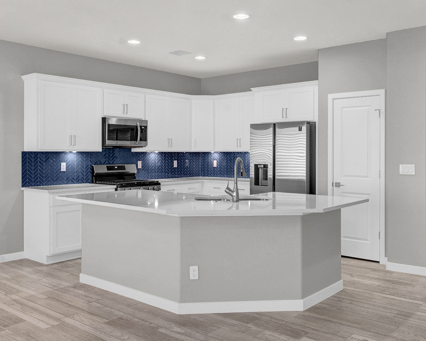Modern kitchen with white cabinets, blue backsplash, and gray island. Stainless steel appliances.
