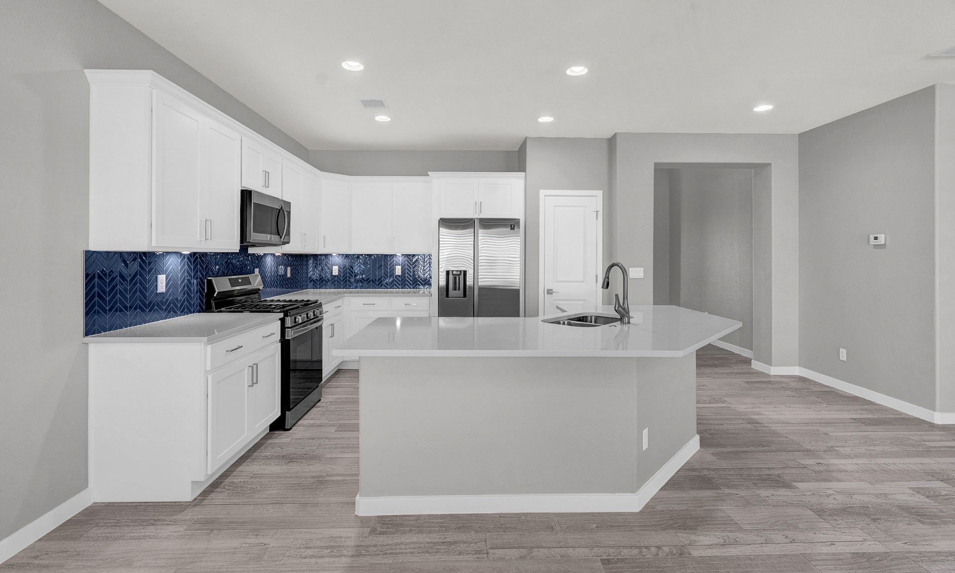 Modern kitchen with white cabinets, blue backsplash, and gray island.