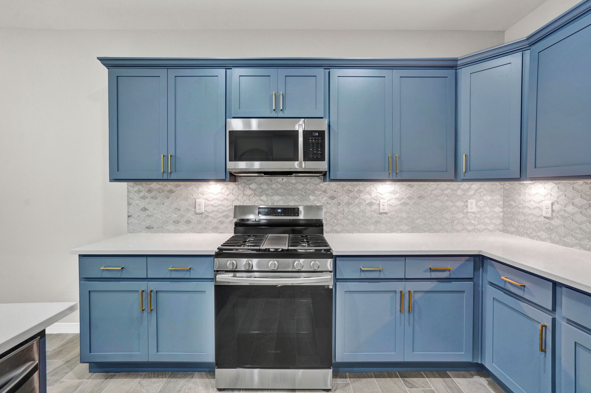 Blue kitchen cabinets with stainless steel appliances and white countertops.