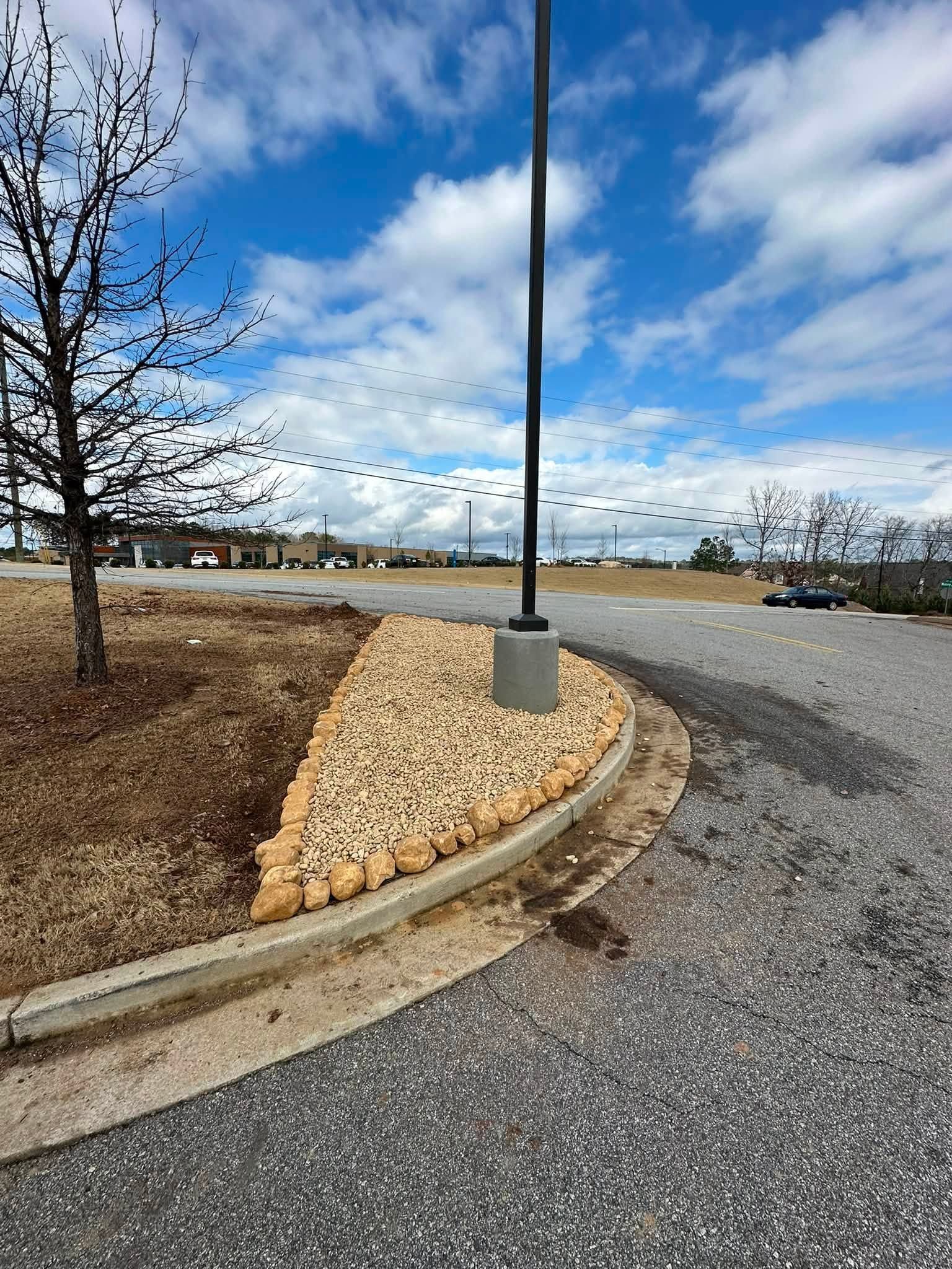 Parking lot curb island with rocks and a tall light pole under a cloudy blue sky