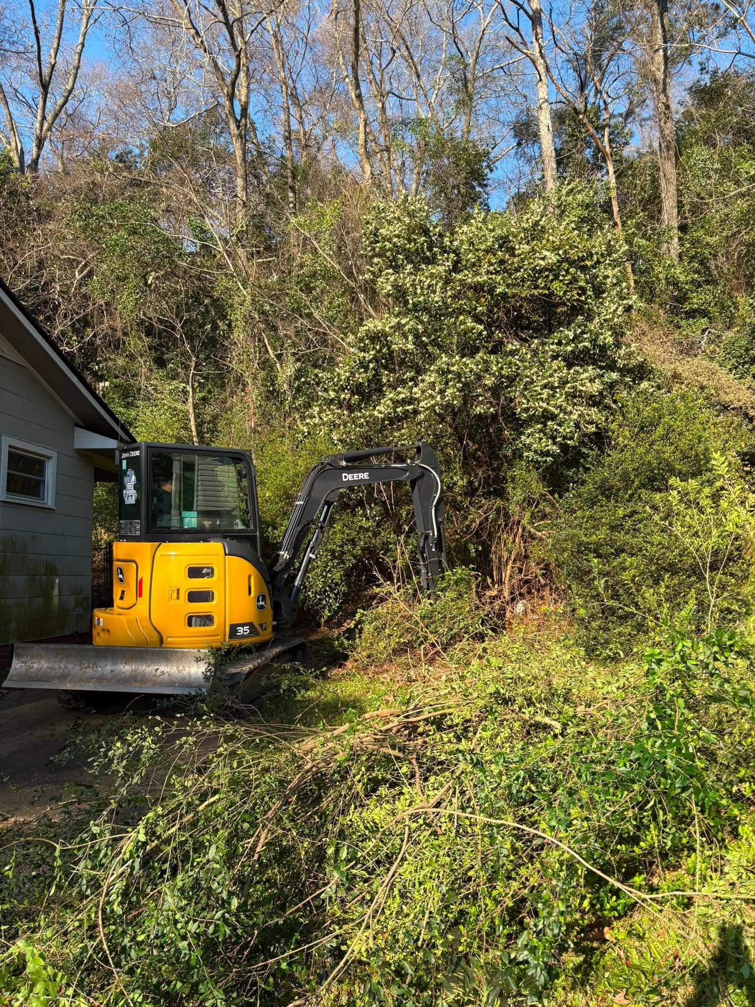 Mini excavator digging a landscaped yard beside a tree and wooden deck on a sunny day