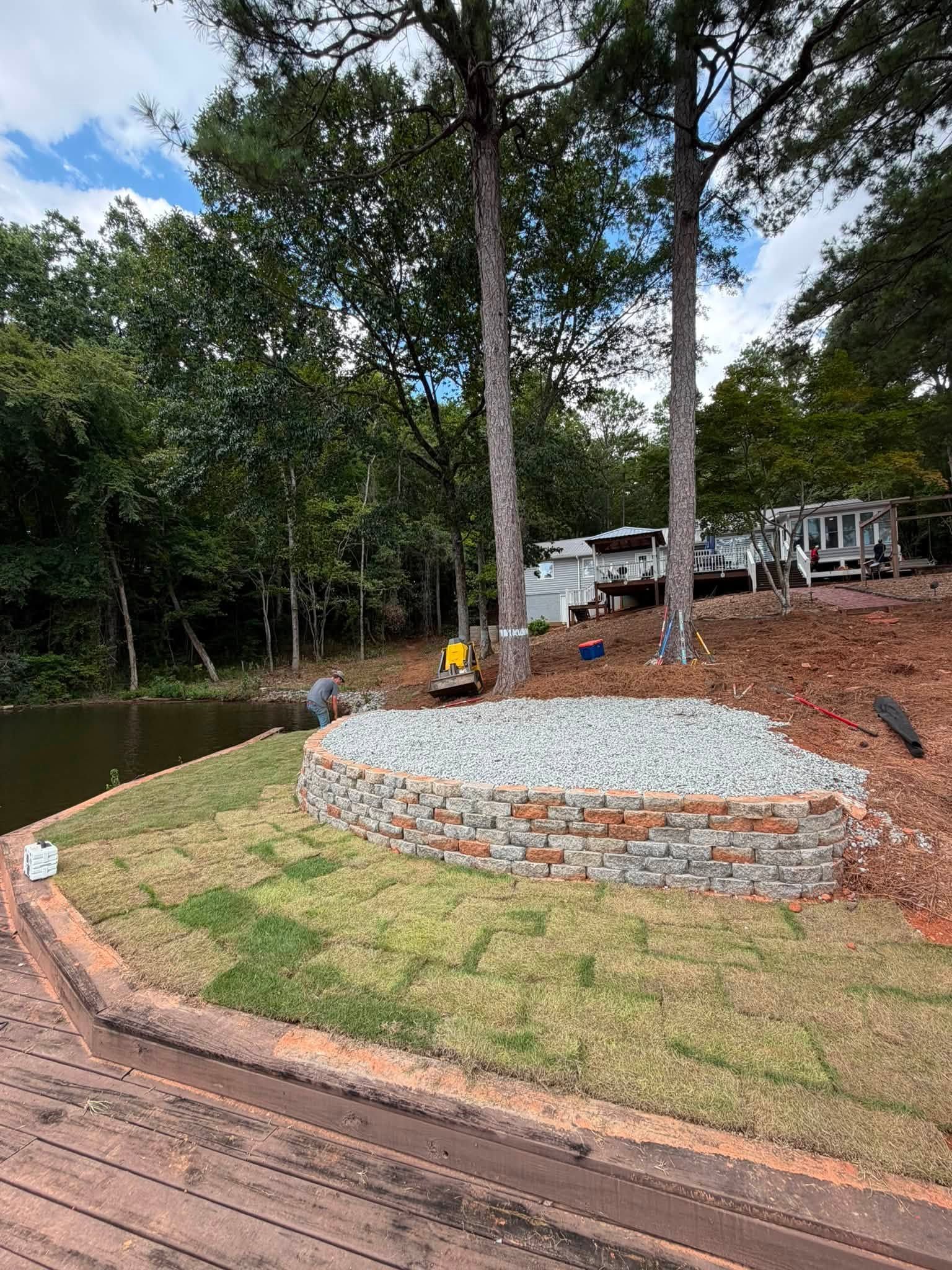 Wooded riverside with a stone fire pit, wooden deck, and a small dock by calm water