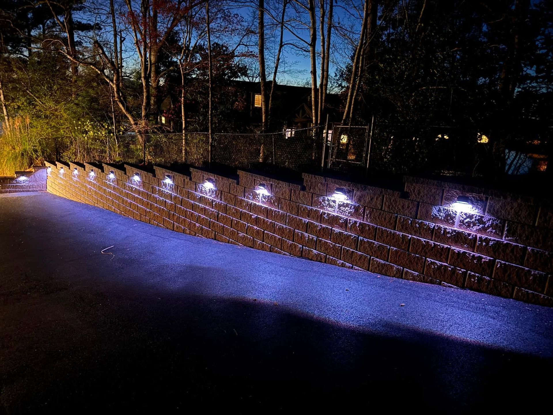 Night scene of a brick wall with purple-white lights and water cascading down into a dark pool