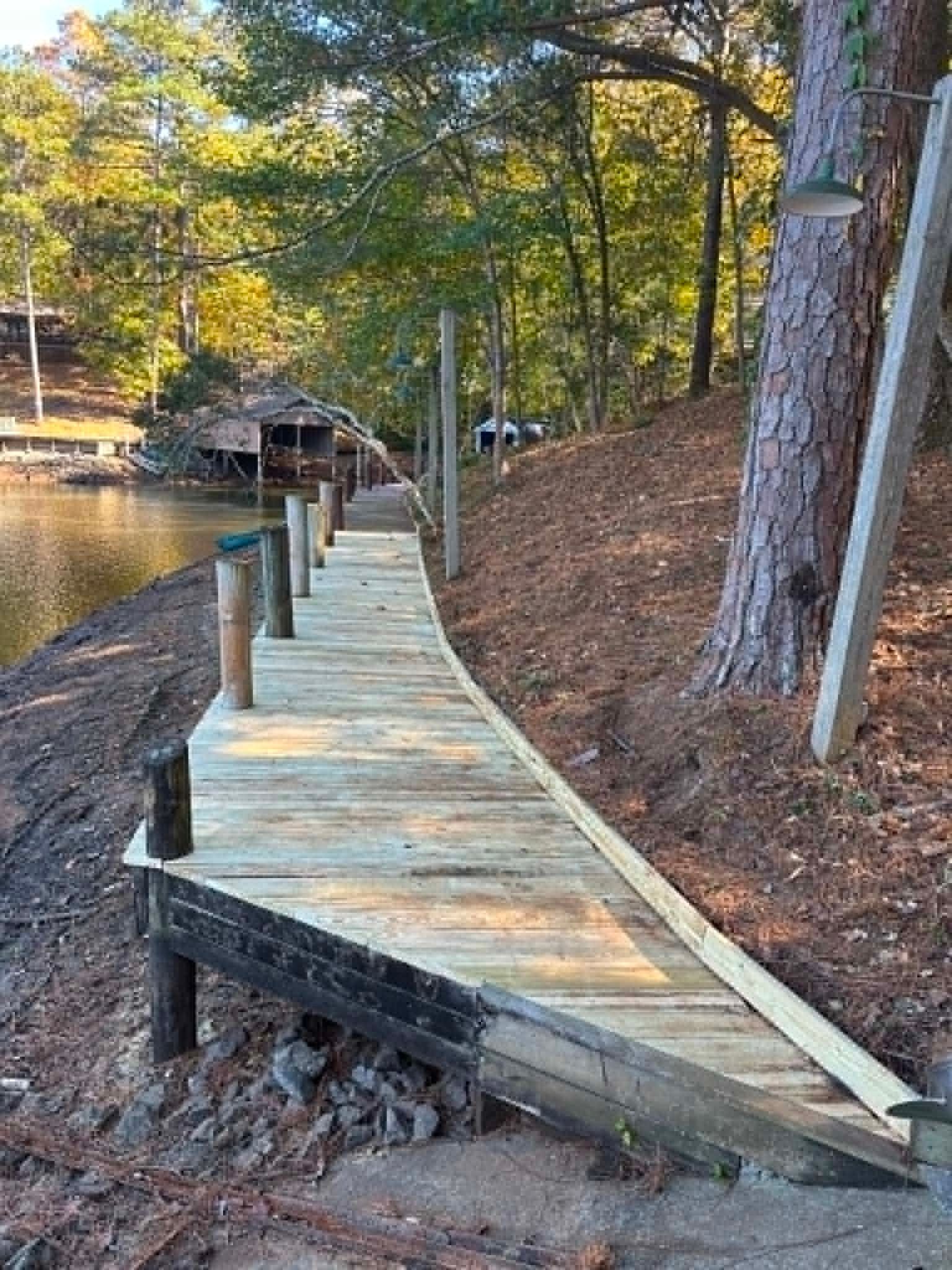 Wooden boardwalk along a lakeshore with a bent ramp and trees in autumn light