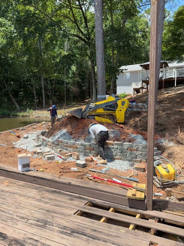 Construction workers excavating a demolished patio beside a house with a yellow mini excavator.