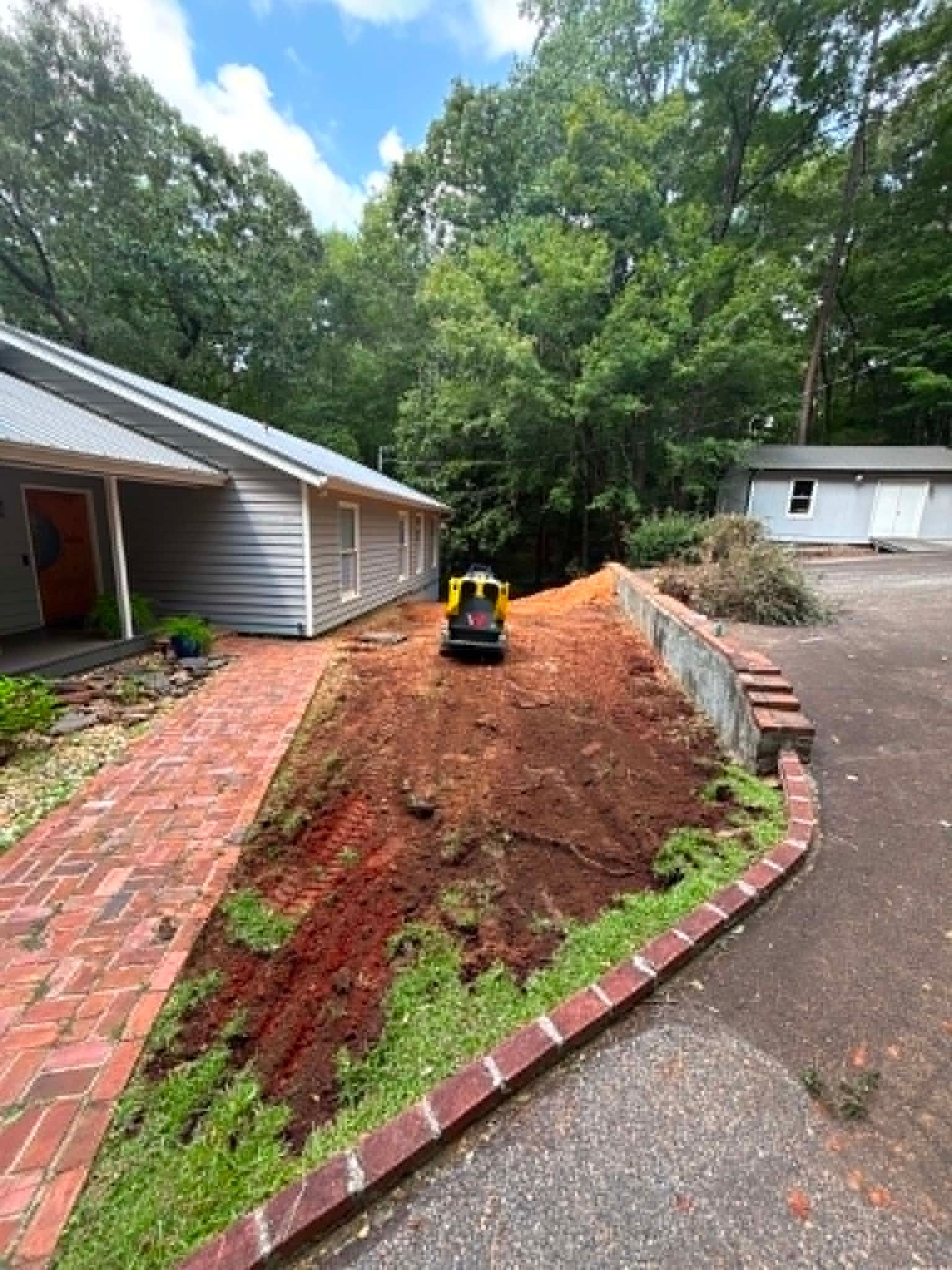 Landscaped front yard with fresh red soil, brick border, and a small yellow excavator beside a house