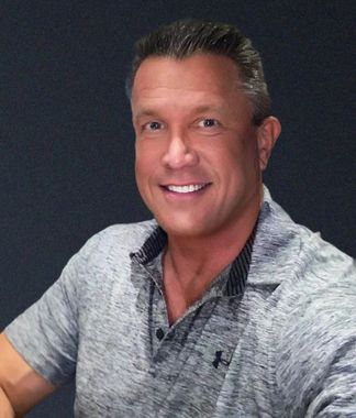 Smiling man in a gray shirt seated against a dark background