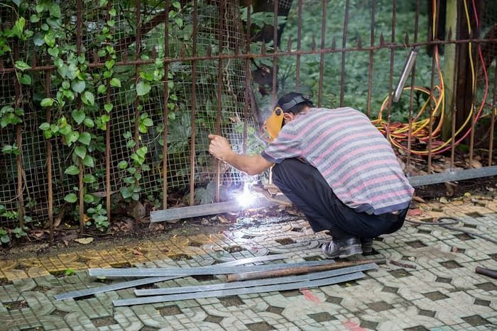 A Person in a Striped Shirt Squats on a Paved Path — A Betta Fence 'N' Yard In Port Macquarie, NSW