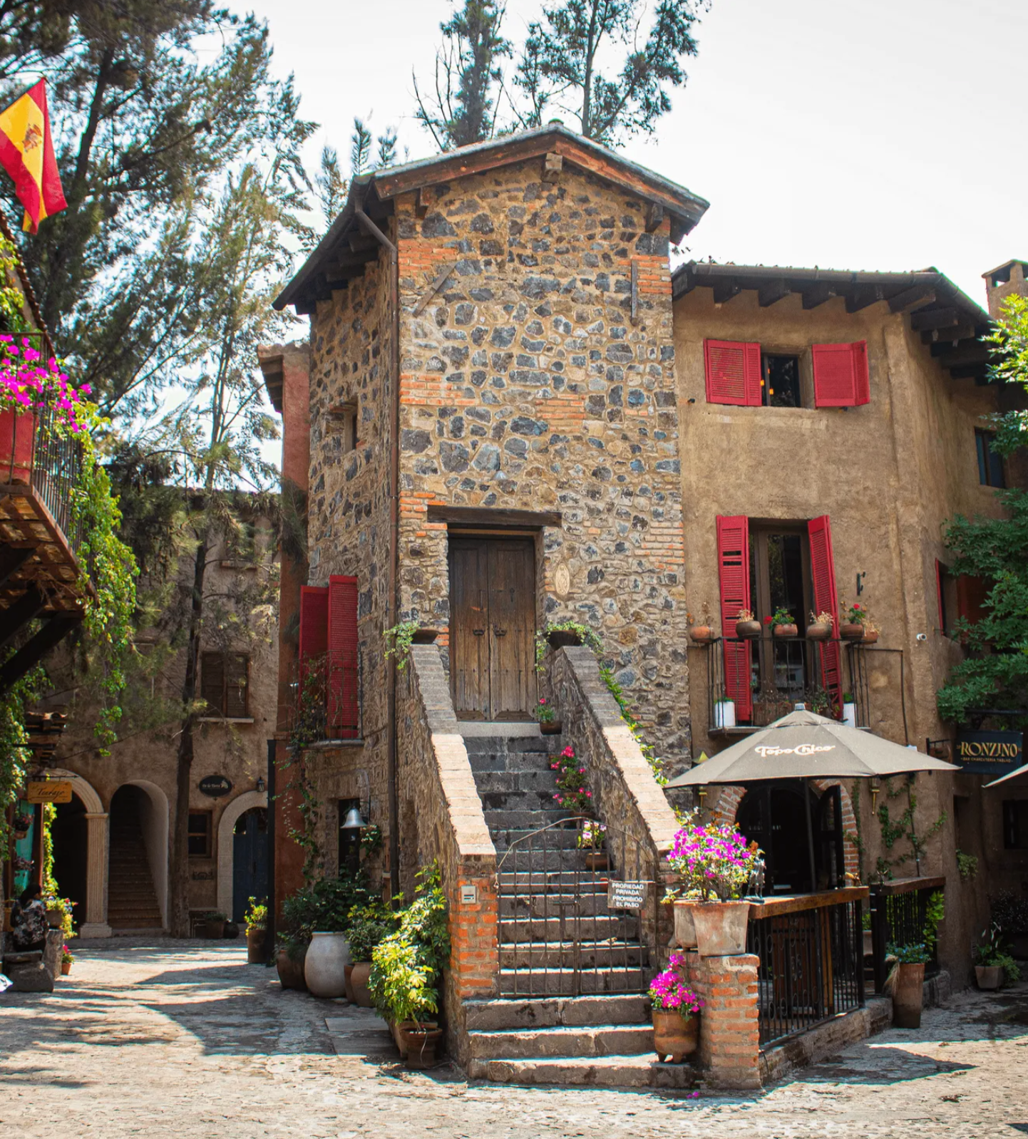 Stone building with red shutters and staircase in a quaint cobblestone courtyard