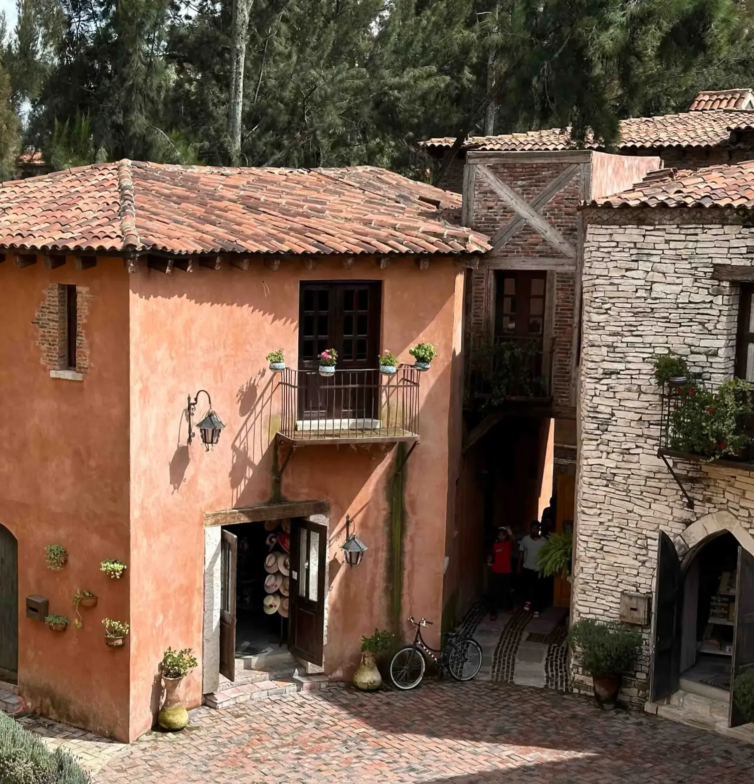 Rustic stone and stucco buildings with red-tiled roofs lining a narrow courtyard lane