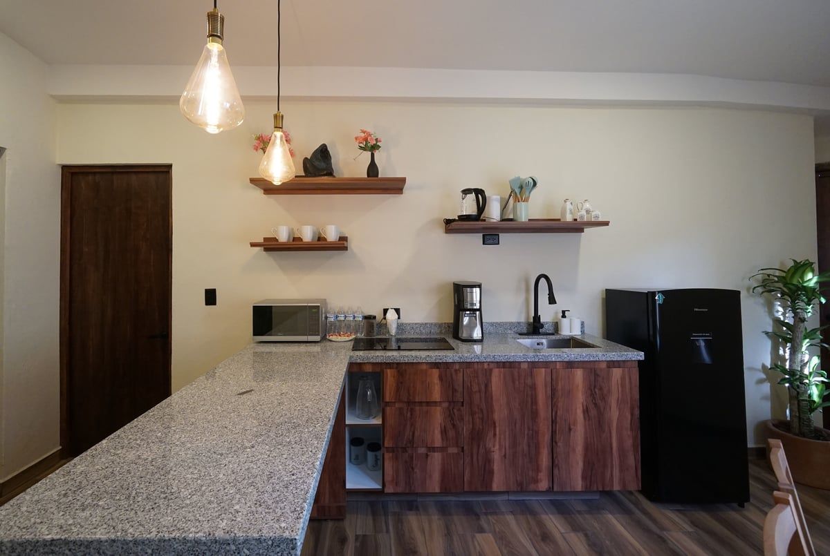Modern kitchen with granite island, wood cabinets, open shelves, pendant lights, and a black fridge