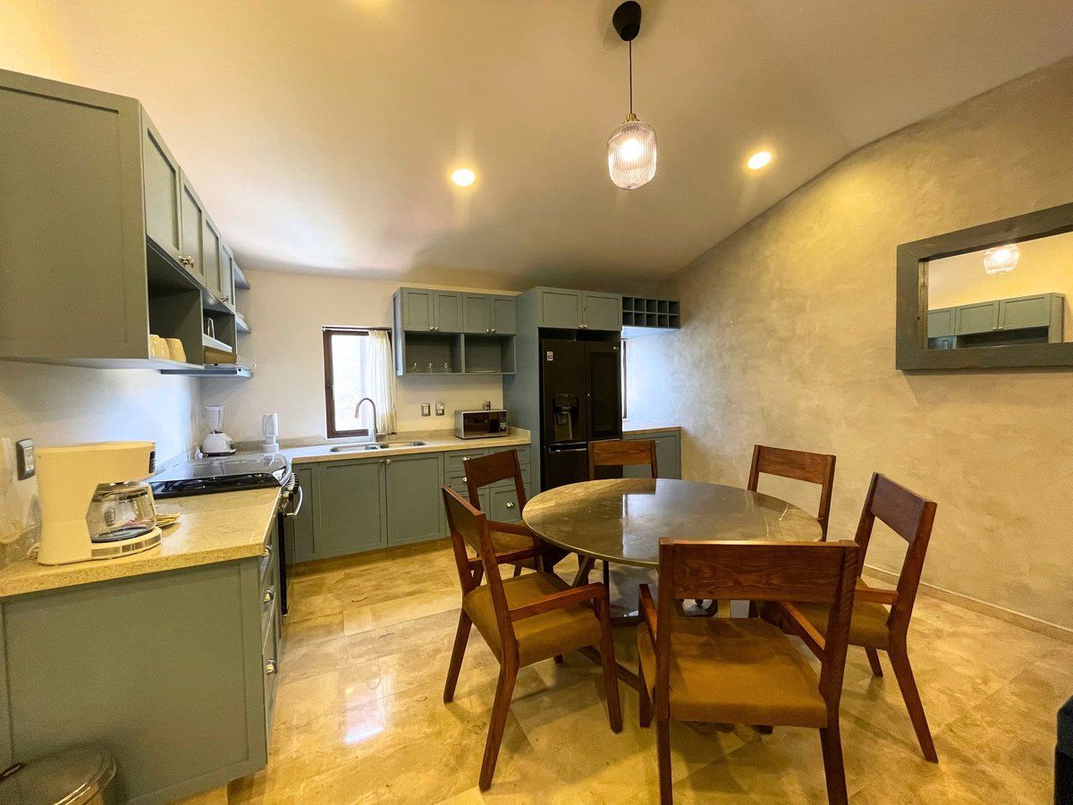 Dining area with wooden table and chairs in a small kitchen, warm lights, and beige walls.