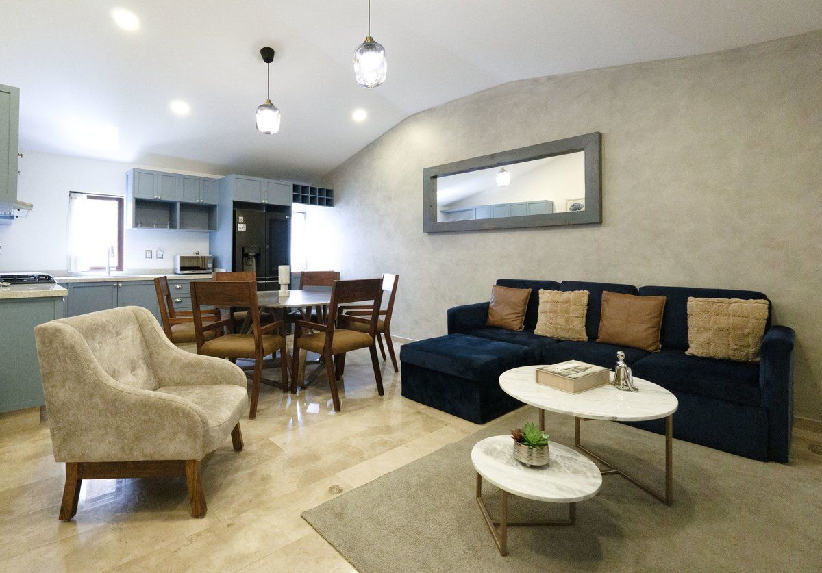 Modern living room with navy sofa, beige chair, round coffee table, dining area, and open kitchen