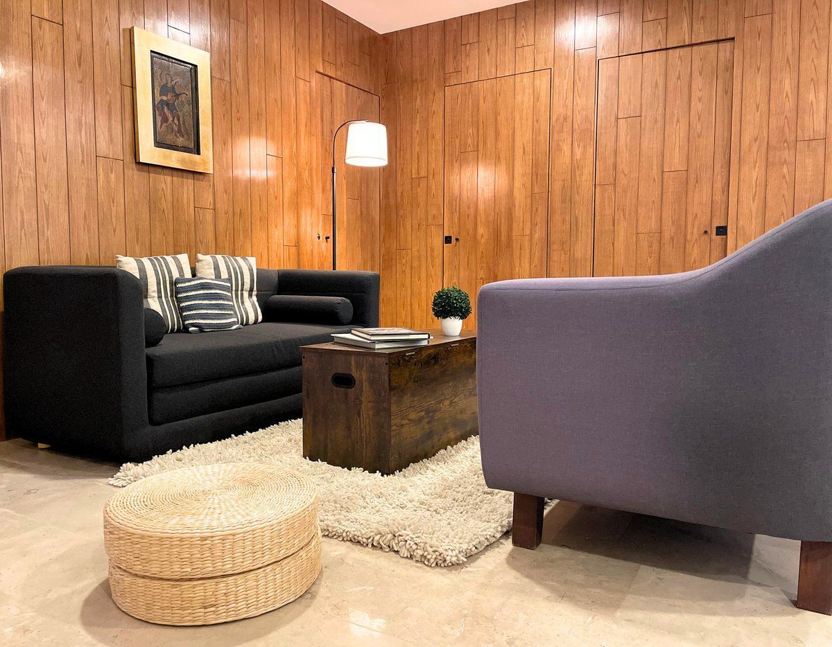Cozy living room with black sofa, lavender chair, wooden coffee table, and rustic wood-paneled walls
