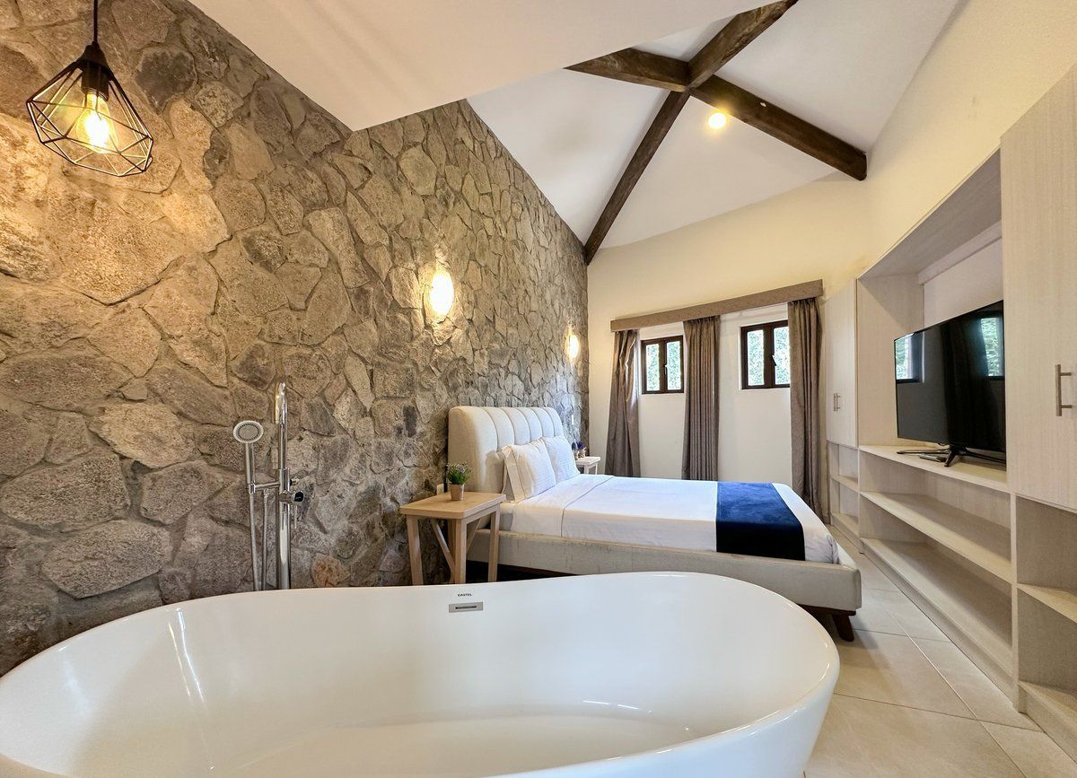 Modern bedroom with stone accent wall, exposed beams, bathtub, and large bed