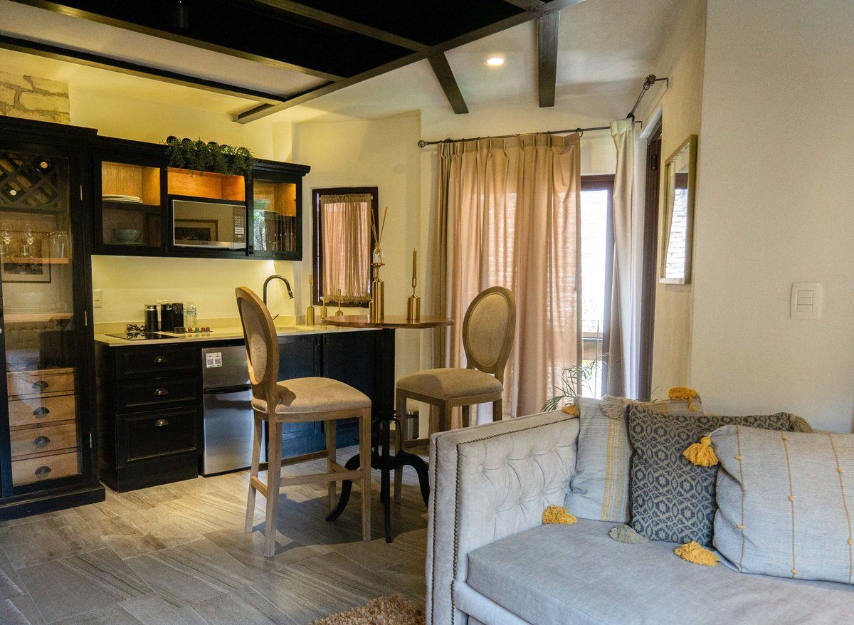 Small open-plan living room with gray sofa, dining table, and kitchen bar stools by sliding curtains.