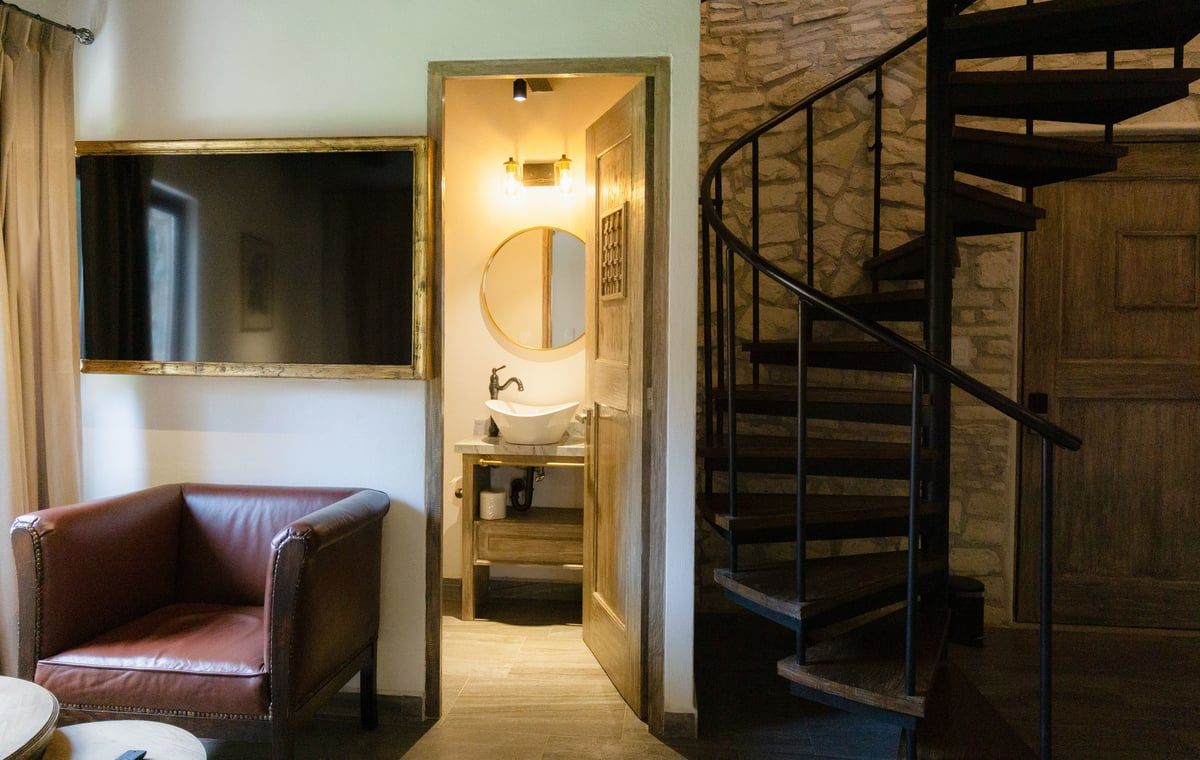 Small interior with a leather chair, bathroom doorway, and spiral staircase in warm light