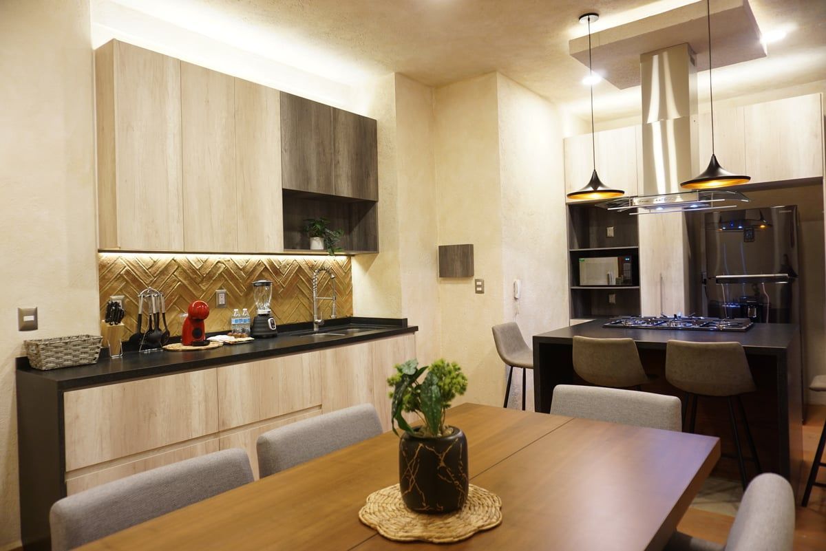 Modern kitchen and dining area with wooden table, light cabinets, black countertops, and pendant lights.