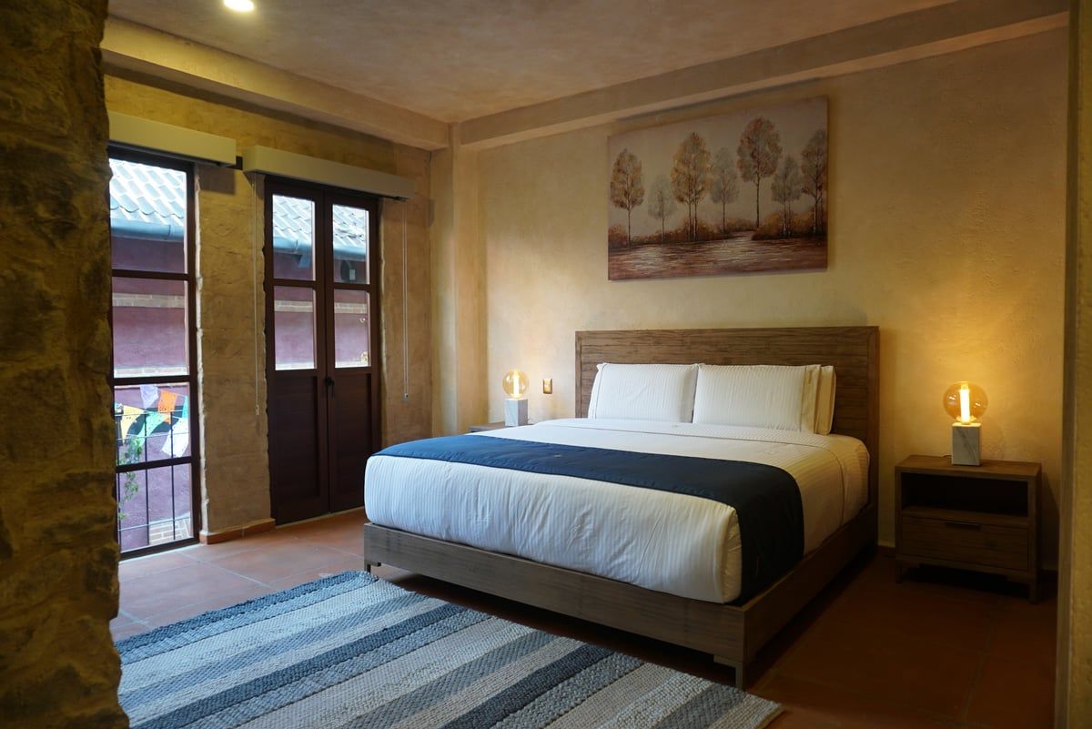 Modern bedroom with a king bed, bedside lamps, wall art, and balcony doors with sheer curtains