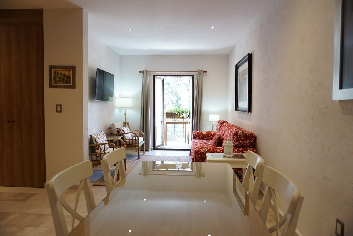 Bright modern living room with white chairs, red sofa, wall art, and sliding doors to a sunny balcony
