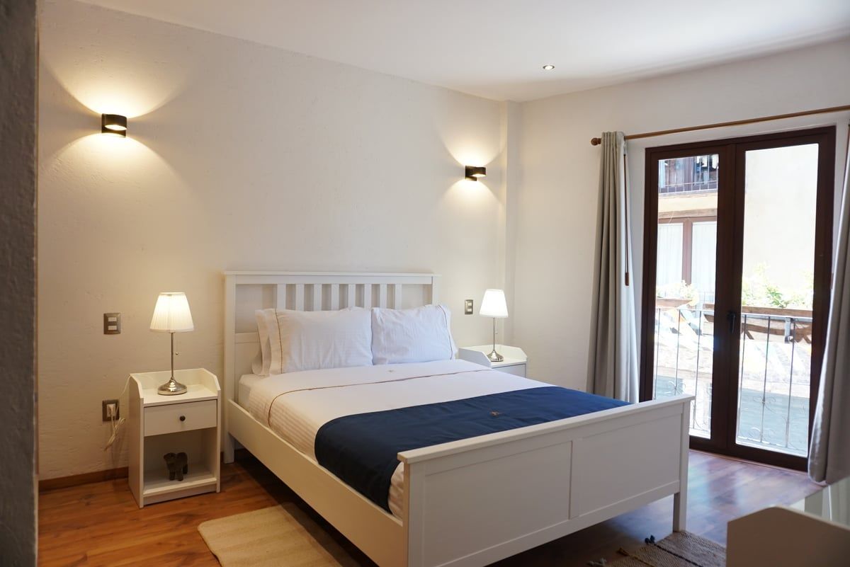 Bright bedroom with white bed, bedside lamps, and open balcony doors letting in daylight