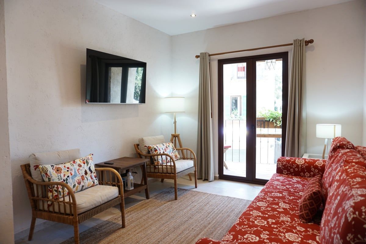 Bright living room with wicker chairs, red sofa, wall-mounted TV, floor lamp, and glass doors to a balcony