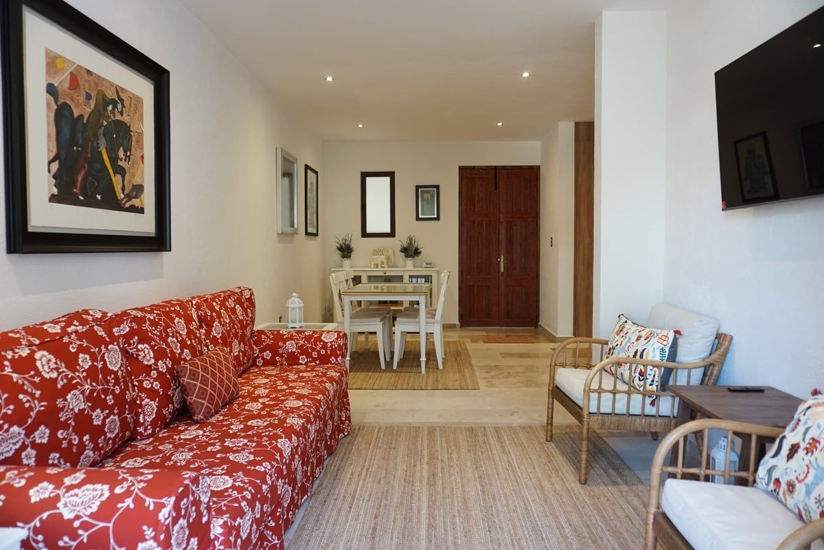 Living room with red floral sofa, dining table, wicker chairs, and wall-mounted TV