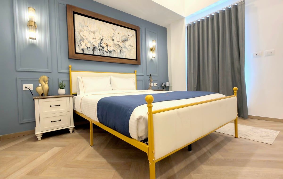 Bright bedroom with a white bed, blue accent wall, gold frame, and gray curtains