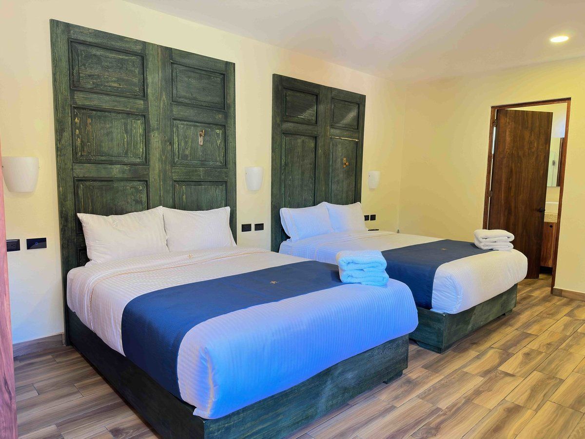 Hotel bedroom with two beds, blue blankets, green shutters, and wood flooring