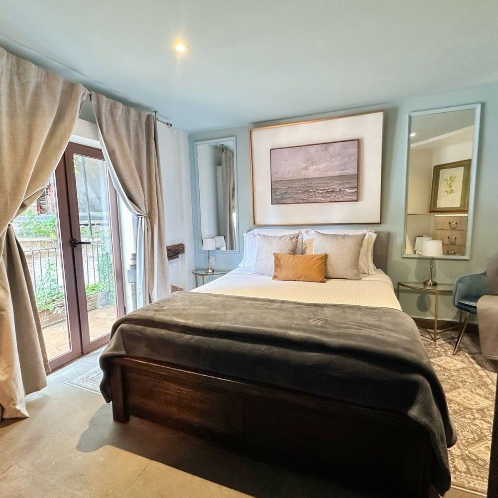 Bright bedroom with a bed, mirrored nightstand, and curtains by a window balcony door