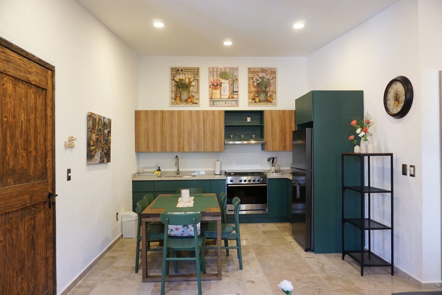 Small modern kitchen with green cabinets, dining table, and teal refrigerator in a bright room.