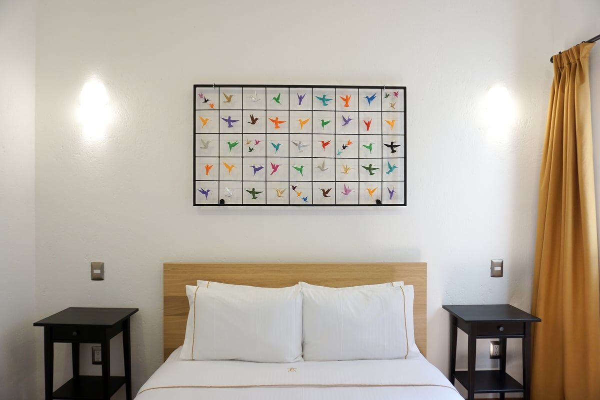 Minimal bedroom with white bed, wood headboard, black side tables, and colorful framed wall art