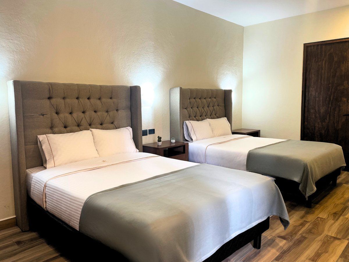 Hotel room with two twin beds, gray bedding, tufted headboards, and warm lighting