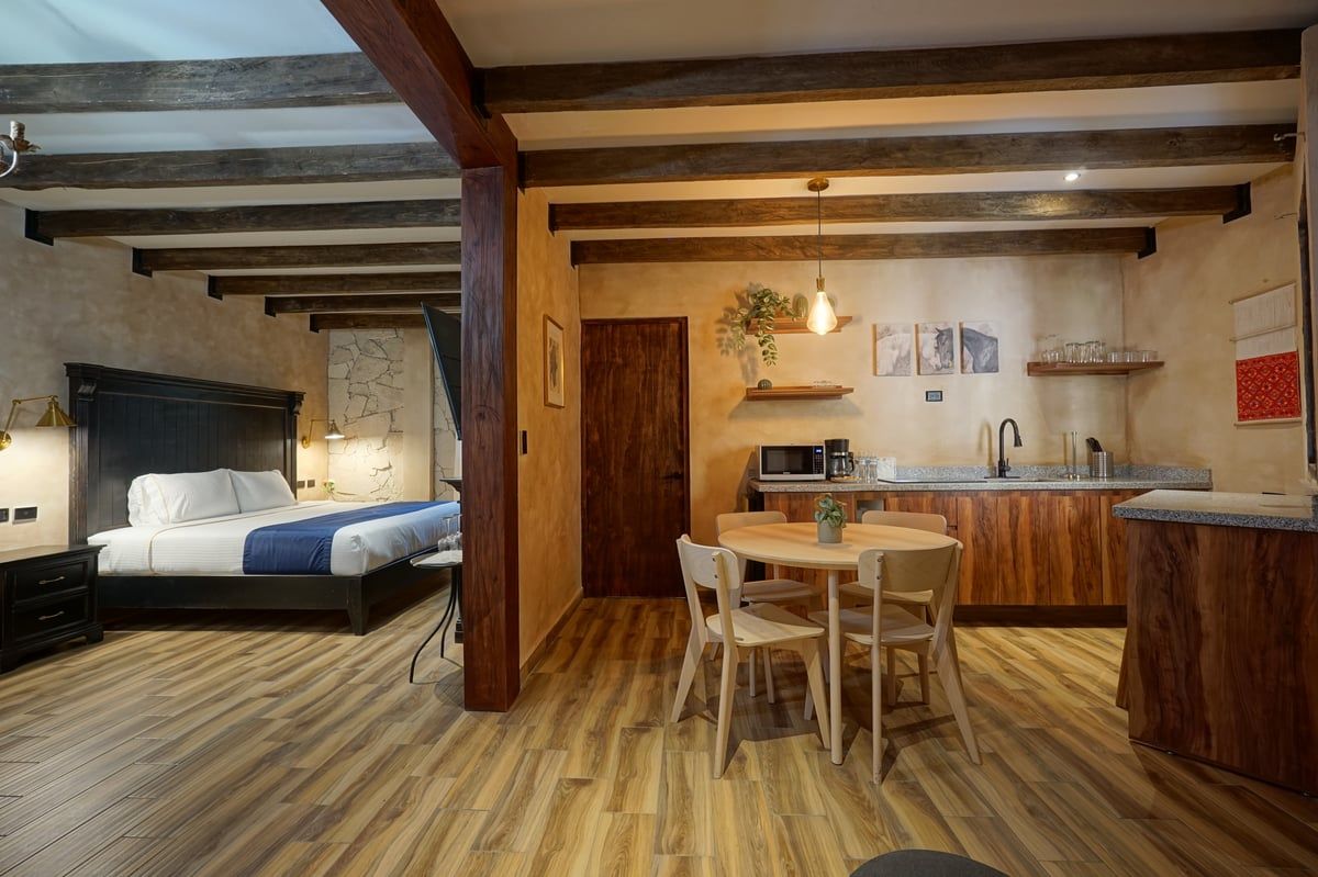 Rustic studio room with bed, dining table, and kitchen area under wooden beams