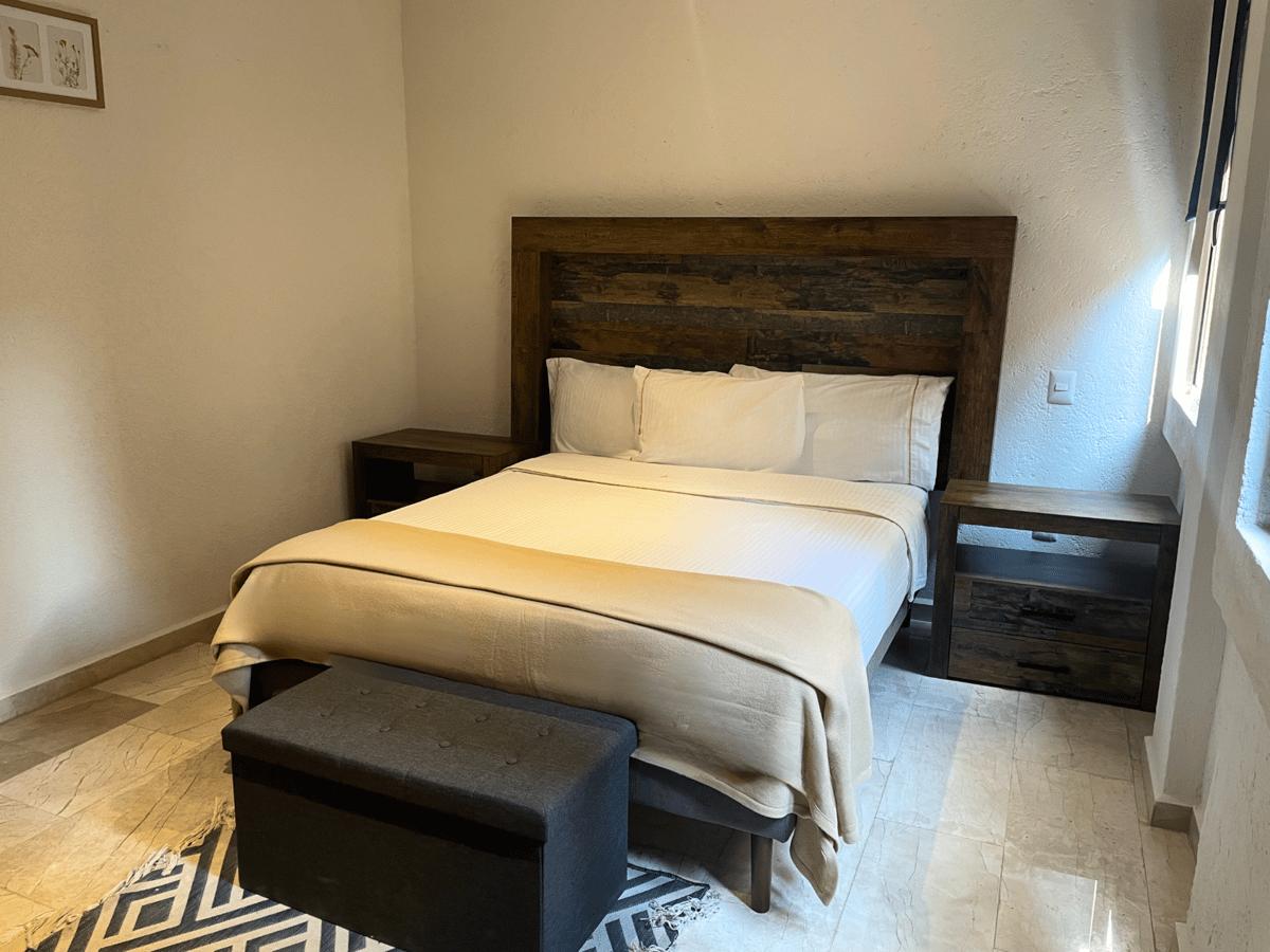 Bedroom with a bed, wooden headboard, white bedding, and gray bench near the foot of the bed.