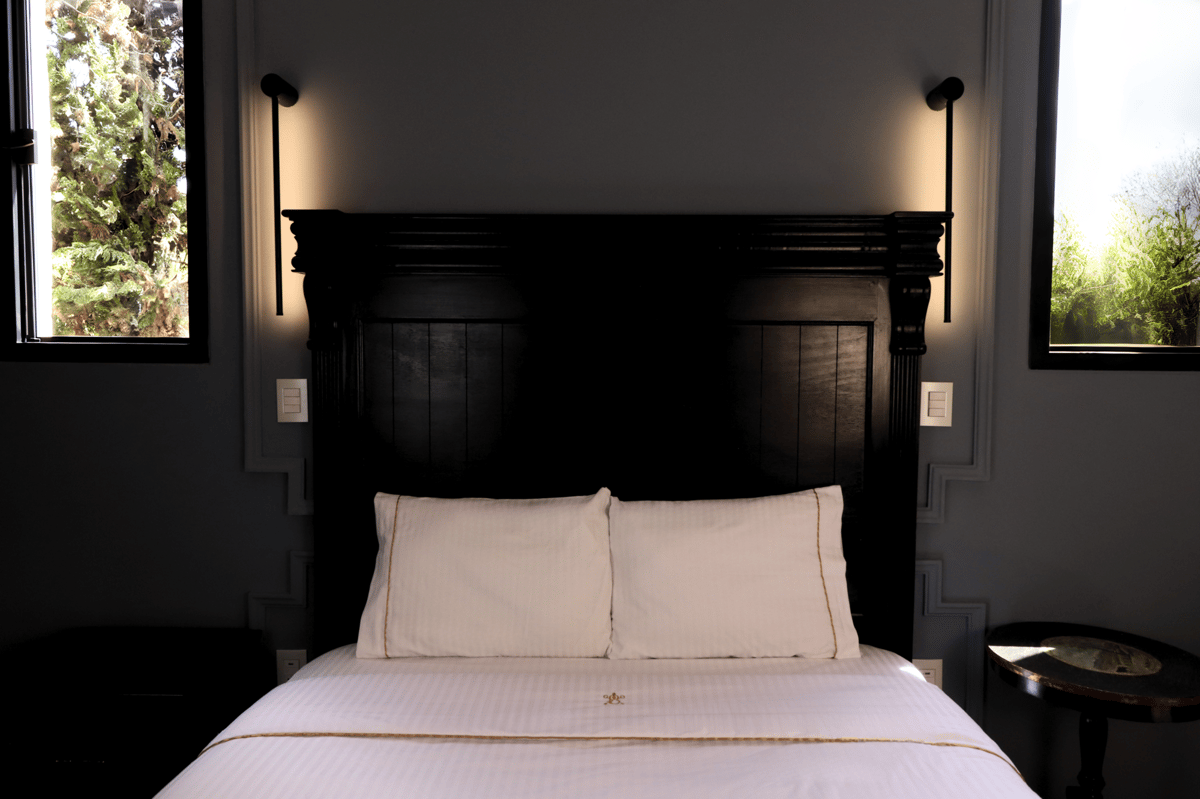 Neatly made bed with white pillows and dark wood headboard in a dimly lit bedroom