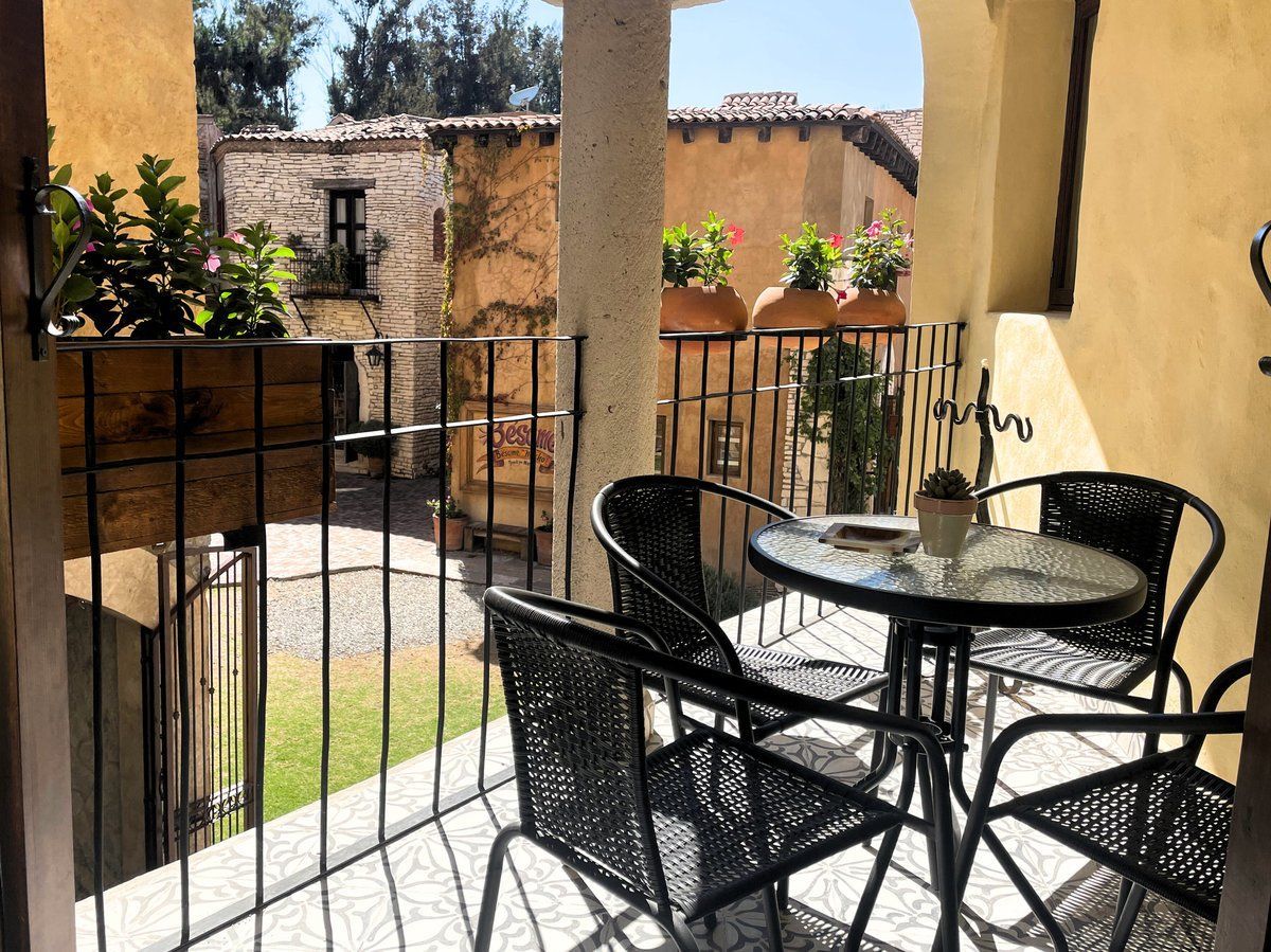 Patio with black metal table and chairs, overlooking a sunny courtyard with stone walls and potted plants