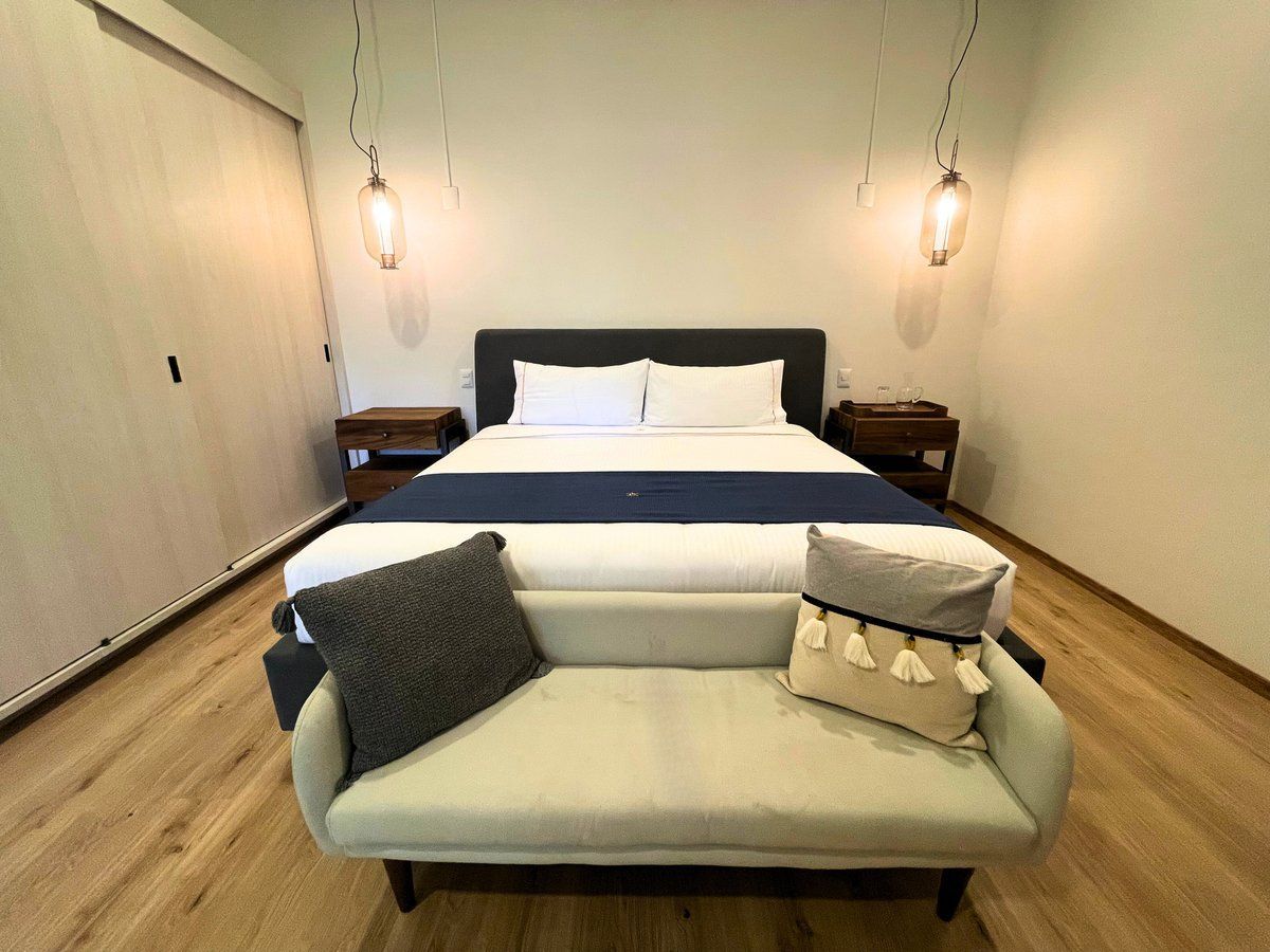 Modern bedroom with a bed, bench, nightstands, hanging lights, and wood flooring