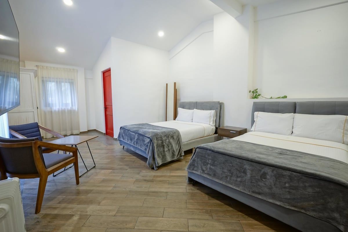 Modern bedroom with two beds, wooden floor, and a small desk by a curtained window.