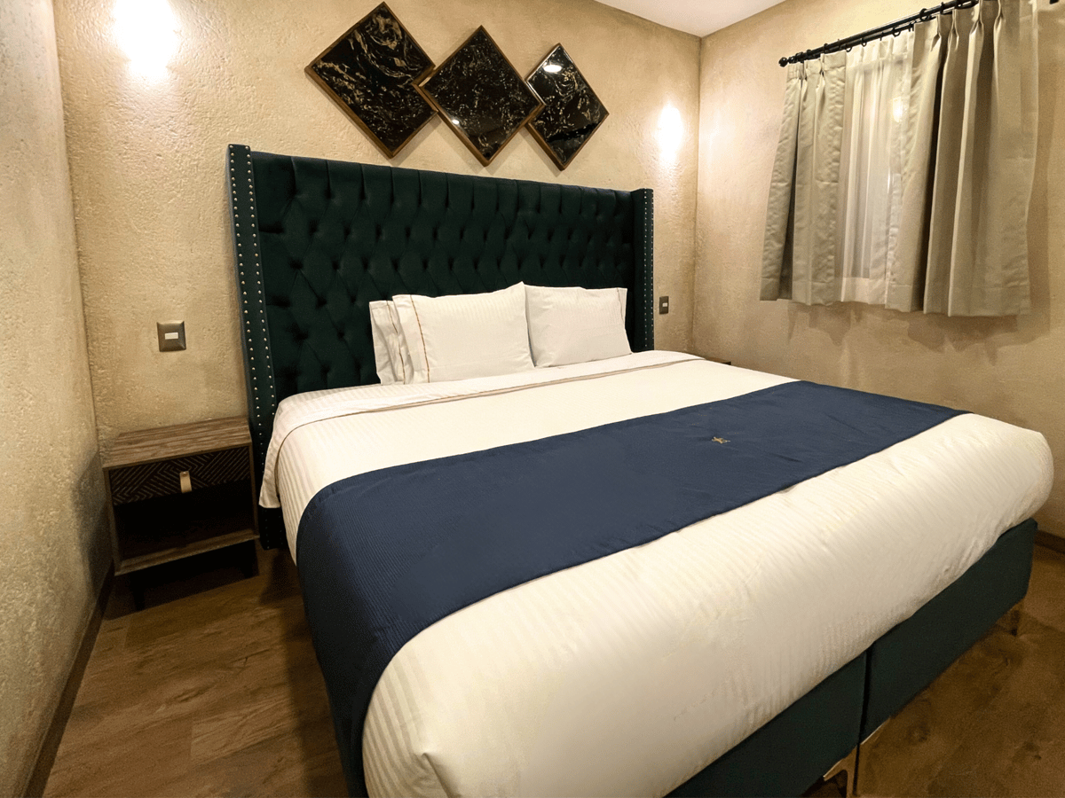Bedroom with a king bed, dark teal headboard, beige walls, and framed wall art.